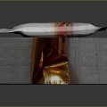 Delicious Chocolate Bar With White Wrapper And Red Gold Accents Placed On Textured Silver Box