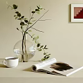 Transparent Glass Vase with Green Leaves and White Coffee Cup Open Magazine on Neutral Table