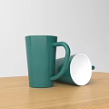 Green Ceramic Mugs One Standing One Toppled On Wooden Table With White Background