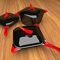 Three Black Cookware Pieces With Red Handles And Lids On Wooden Table