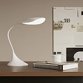 Modern White Desk Lamp With Curved Design On Wooden Table Beside Collage Wall Art