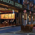 Commercial Street With Starbucks Coffee Shop Outdoor Seating Evening Lights Storefronts Tables Chairs And Flower Pots