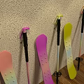 Pink Purple Yellow Snowboards And Ski Poles Leaning Against Wall On Wooden Floor