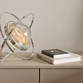 Modern Orbital Design Table Lamp With Metal Frame And Glass Globe On Tabletop With Books