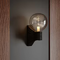 Black Spiral Wall Lamp with Transparent Globe Shade Glowing Bulb on Grey Wall Wooden Panel