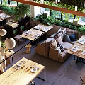 Open Restaurant Interior With Lush Greenery Natural Light Cozy Seating And Wooden Dining Tables
