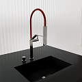 Modern Kitchen Faucet With Red Curved Spout And Chrome Base On Black Countertop With Sink