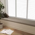 Decorative Pillows on Cozy Window Seat with White Blinds Green Plant and Open Magazine Nearby