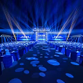 Formal Event Venue With Blue Lighting Rows Of Chairs And Stage Screens