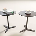 Two Modern Circular Side Tables With Black Legs Holding Coffee Cups And Books