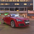 Red Audi Sports Car Parked On Urban Street With Tall Buildings And Evening Lights