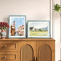 Two Blue Picture Frames With Scenic Paintings On Wooden Cabinet And Red Flower Vase