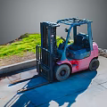 Pink Forklift Parked On Concrete Ground With Grass Area And Extended Forks