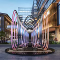 Illuminated Circular Ring Landscape Sculpture In Commercial Area Square With Modern Buildings And Greenery