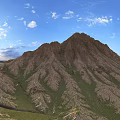 Scenic Mountain Landscape With Rolling Brownish Yellow Peaks Green Grass Blue Sky And White Clouds