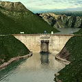 Massive Concrete Hydroelectric Dam Nestled In Lush Green Mountain Valley With Calm Clear Reservoir Water
