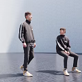 Two Men In Black Striped Outfits Standing And Sitting With Light Shoes On Dark Floor
