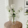 White Flowers With Green Leaves In Glass Vase On Wooden Round Table