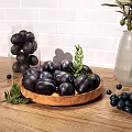 Black Fruits on Wooden Plate with Green Leaves Scattered Small Fruits Near Transparent Vase