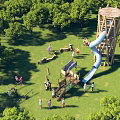 Outdoor Playground With Wooden Slide Tower Green Grass Trees And People Playing