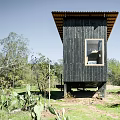 Black Wooden Guesthouse Building Exterior With Large Windows And Hillside Greenery