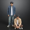 Two Young Men Standing and Sitting in Casual Outfits Against Gray Background