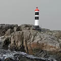 Red And Black White Lighthouse Tower Standing On Rocky Coastal Area