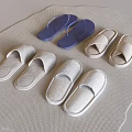 Multiple pairs of soft indoor slippers in white light gray and blue on woven mat