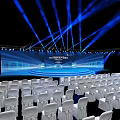 Modern Conference Hall Setup With White Chairs Stage Screen And Blue Lighting