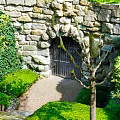 Garden Landscape With Vine Covered Stone Wall Iron Gate Trimmed Bushes And Gravel Pathway