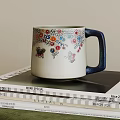 Ceramic Mug with Colorful Floral Patterns Butterflies and Blue Handle Placed On Stacked Magazines