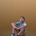Young Man Sitting On Ground With Blue T-Shirt And Khaki Shorts Against Brown Background