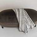 Dark Brown Oval Upholstered Ottoman With Light Gray White Striped Knitted Blanket