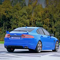 Stylish Blue Jaguar Sedan With Sleek Design And Green Trees Background