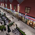 Vibrant Commercial Street With Red Roof Buildings Shops Outdoor Seating Green Plants And String Lights