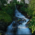 Scenic Natural Waterfall Scene With Flowing Blue Water Lush Green Vegetation And Rocks