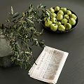 Decorative Ornament Arrangement With Green Vase Olive Branches Black Plate Green Apples And Newspaper