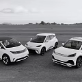 Three White Electric Vehicles Parked On Open Ground With Scenic Background