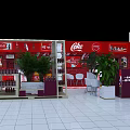 Coca Cola Display Area With Red Background Shelves Drinks Green Plants And White Chairs