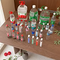 Assorted Bottled Drinks and Water Bottles on Wooden Table with Green Plants and Red Fruits