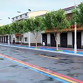 Scenic Commercial Street With Trees Buildings Pedestrians And Car On Colorful Road Lanes