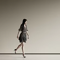 A Woman Walking Against Beige Background Wearing Dark Dress High Heels and Long Black Hair