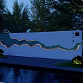 Scenic Feature Wall With Wavy Design Illuminated At Night Surrounded By Trees And Water