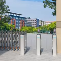 Entrance Gate With Automatic Turnstiles Flanking Pillars Surrounding Trees And Background Buildings Under Blue Sky