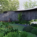 Serene Relaxation Area With Lush Green Plants Stone Wall Fountain And Round Shrubs