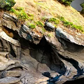 Natural Rocky Terrain Featuring Layered Rock Formations Cliffside Vegetation And Caves
