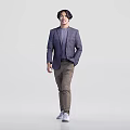 Man In Purple Plaid Blazer Gray Top And Brown Pants Stands Naturally Against Gray Background