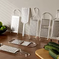 Stainless Steel Kitchen Graters on Wooden Table with Green Apples Zucchini and Cutting Board