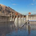 Large Industrial Plant Dam Structure With Water Flow And Orange Equipment Against Mountain Landscape