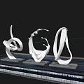 Three Silver Metal Abstract Curved Sculptures on Reflective Platform Under Blue Sky with White Clouds